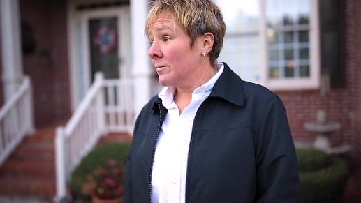 A woman smiles on her front lawn.