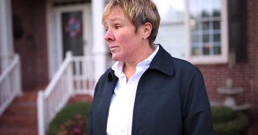 A woman smiles on her front lawn.