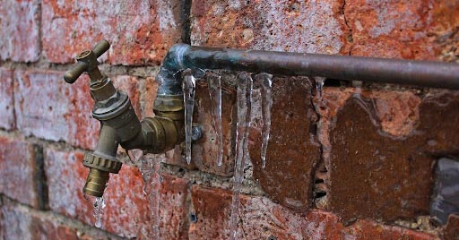 A frozen pipe and spigot on the side of a brick home.