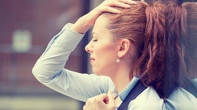 A woman in an office holds her head and appears stressed.