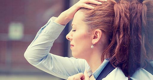 A woman in an office holds her head and appears stressed.